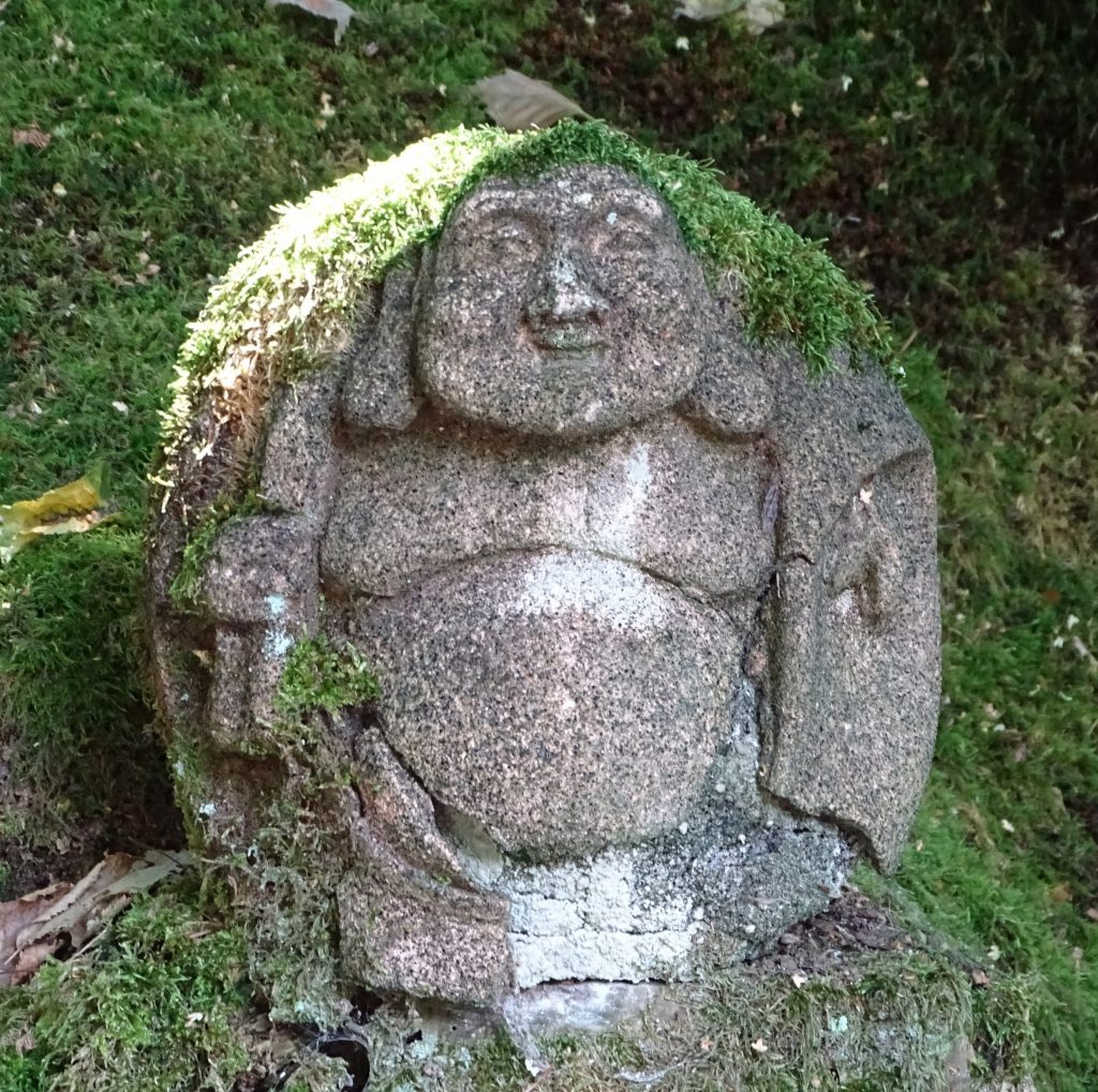 1-Minuten-Trick. Ein steinerner Zen-Mönch in einem Klostergarten, moosbewachsen.